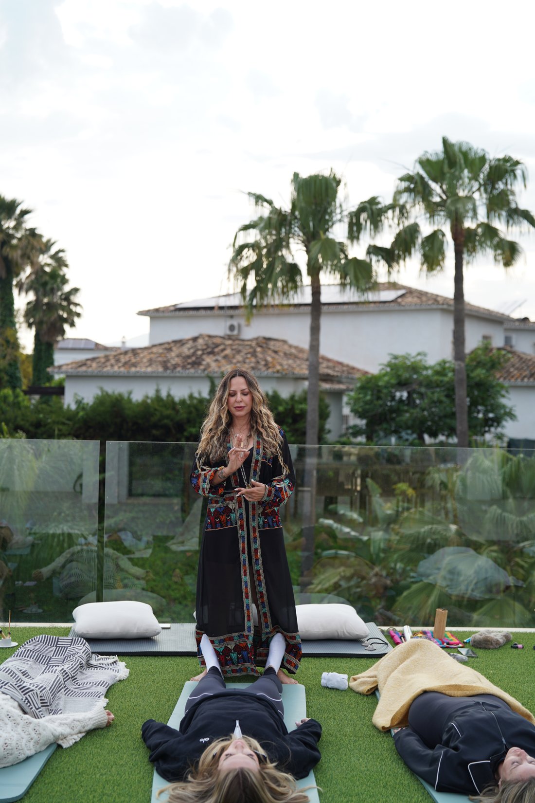 Gishtar guiding an outdoor session over women resting on mats in the garden