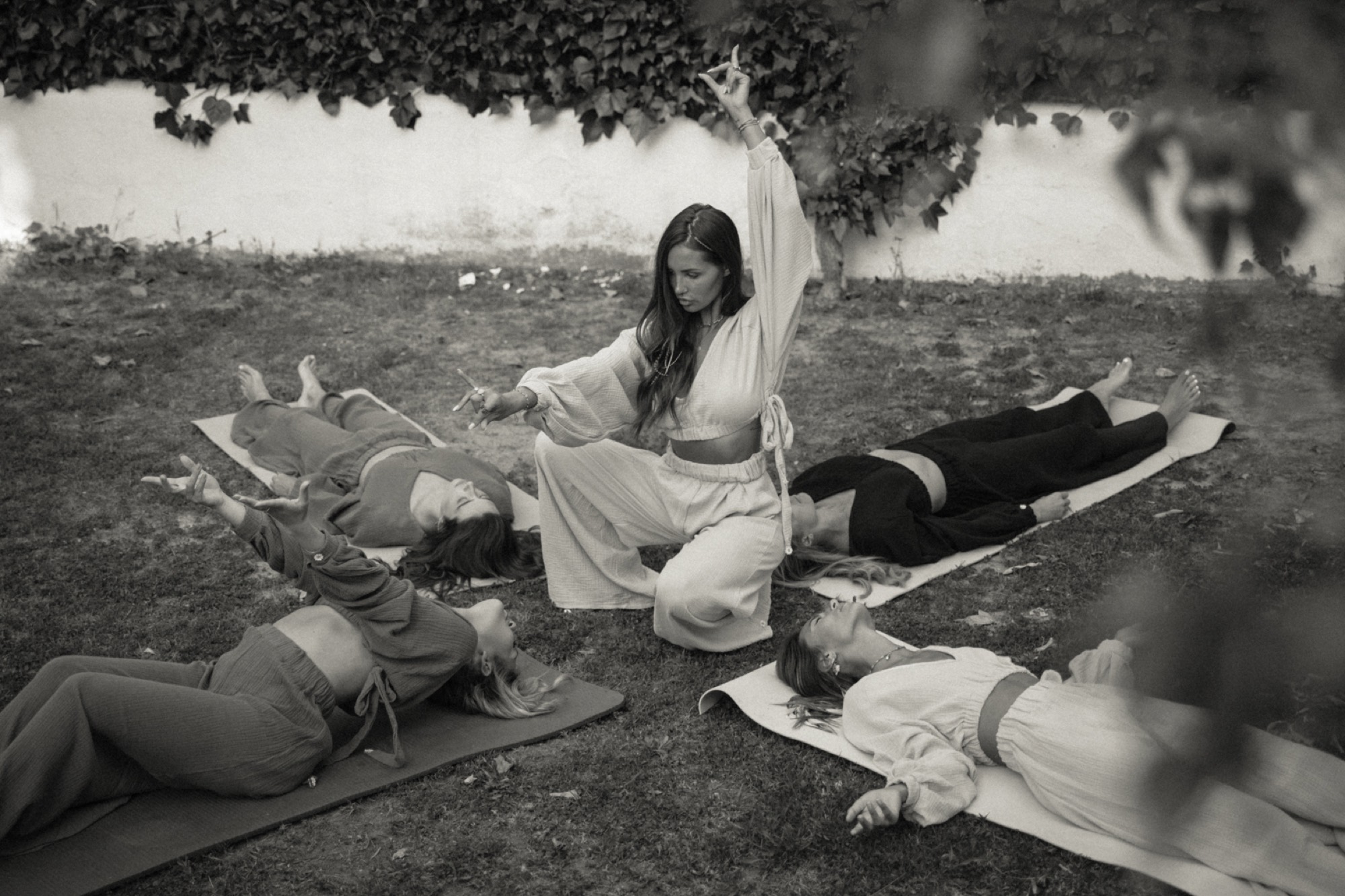 Linnebel guiding a circle of women lying on mats during an outdoor ceremony